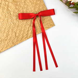 Close-up of bright red satin bow hair clip with long ribbons on elegant gold background