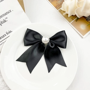 Détail d'une pince à cheveux avec nœud en satin noir et une grande perle blanche centrale