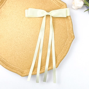 Detail of cream satin double-layered bow hair clip with long ribbons on a tray