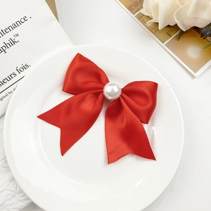 Détail de la pince à cheveux nœud en satin rouge avec perle sur une assiette