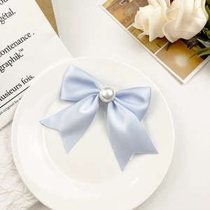 Détail macro du nœud élégant en satin bleu clair orné d'une grande perle sur un plat blanc