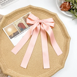 Elegant pink satin bow hair clip with long ribbons on a decorative beige tray
