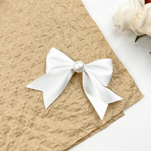 Détail d'une pince à cheveux avec nœud en satin blanc et perle centrale élégante