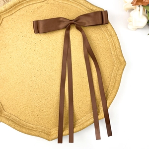 Detail of dark brown satin double bow hair clip with long silk ribbons on a tray