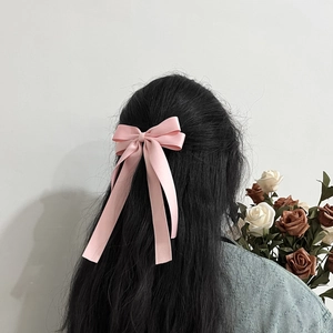Elegant pink satin bow hair clip with long ribbons shown on long dark hair