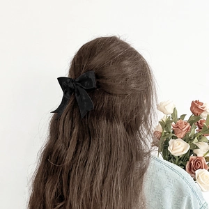 Elegante zwarte fluwelen haarclip met strik voor dames, gedragen in lang golvend haar