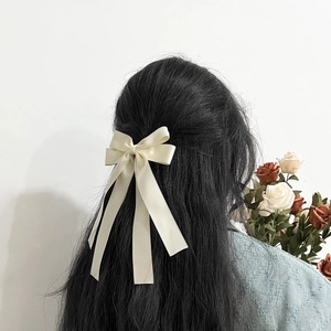 Elegant cream white satin bow hair clip with long ribbons worn on wavy hair