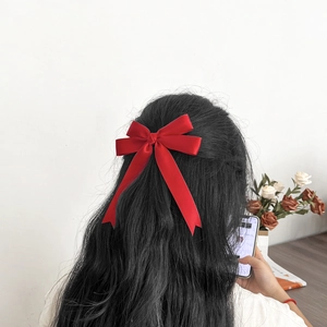 Détail d'une pince à cheveux en satin rouge avec longs rubans sur cheveux noirs