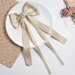 Close-up of elegant champagne satin bow hair clip with long streamers on white plate
