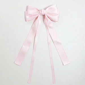Detail of pink satin bow hair clip featuring long flowing ribbons on white background