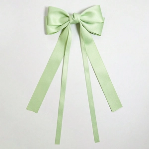Detail of light green satin bow hair clip with flowing ribbons and glossy finish