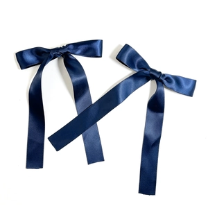 Detail of two dark blue satin bow hair clips with long elegant ribbon streamers