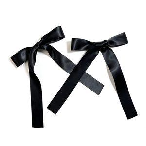 Close-up of a pair of black satin bow hair clips with long silky ribbons on white background