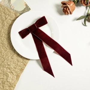 Détail d'une barrette à nœud en velours bordeaux avec longs rubans sur assiette blanche