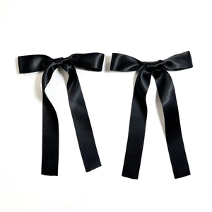 Detail shot of a pair of black satin ribbon bow hair clips with long hanging streamers