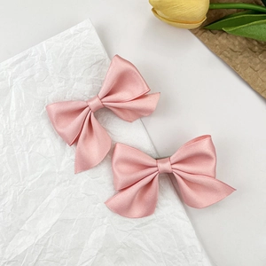 Détail de deux barrettes à cheveux en satin rose avec nœuds sur papier froissé blanc