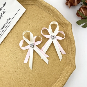Détail des barrettes à nœuds roses et crème avec une pierre précieuse en forme de cœur