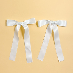 Close-up of two white satin ribbon bow hair clips with long streamers for elegant styling