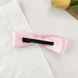 Détail d'un nœud en satin rose avec une pince à bec de canard en métal noir antidérapante