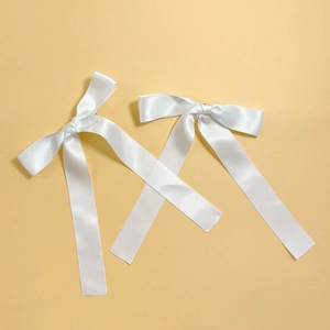 Detail of two white satin bow hair clips with long ribbons and silky smooth texture