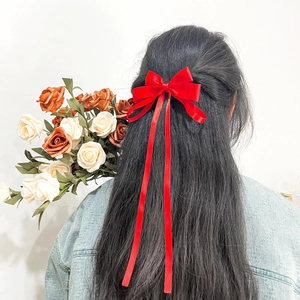 Elegant red satin bow hair clip with long flowing ribbons shown on model's hair