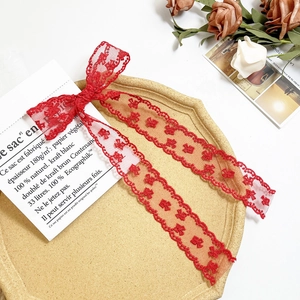 Detailed close-up of a red lace bow hair clip with floral patterns on a stone tray