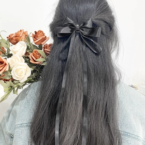 Detail of a black satin double bow hair clip with long ribbons worn on a ponytail