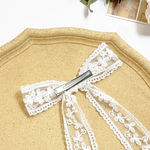 Elegant white lace flower bow hair clip with flowing ribbons on a stylish tray