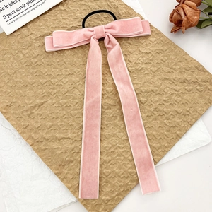 Detailed close-up of pink velvet bow hair tie with long ribbons on retro paper