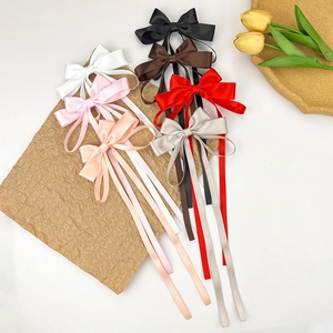 Detailed view of long satin bow hair clips in seven elegant colors on a textured surface