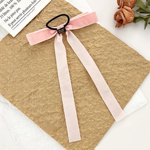 Macro detail of pink velvet bow hair tie with handmade label on vintage paper background