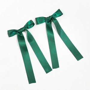 Detail of dark green satin bow hair clips with long ribbons in silky fabric texture
