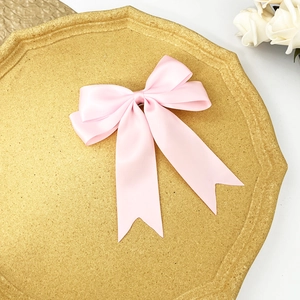 Détail de la pince à cheveux nœud en satin rose avec de longs rubans sur plateau