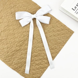 Detail of elegant white satin ribbon bow hair clip with long streamers on brown paper