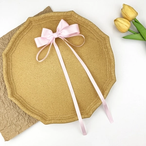 Close-up of a soft pink satin ribbon hair bow with long streamers on a wooden tray