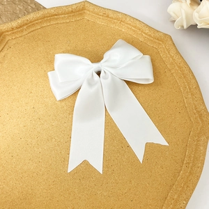 Détail de la pince à cheveux noeud en satin blanc avec longs rubans sur plateau