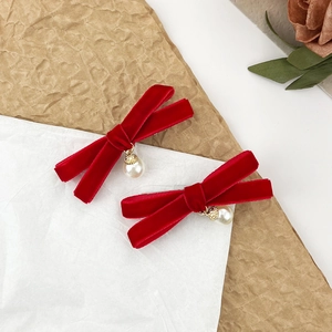 Détail de deux barrettes nœuds en velours rouge avec perles suspendues et accents dorés
