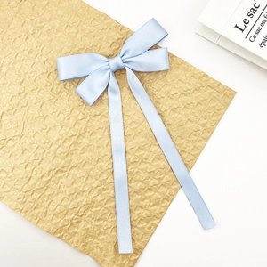 Close-up of light blue satin bow hair clip with long ribbons on textured paper