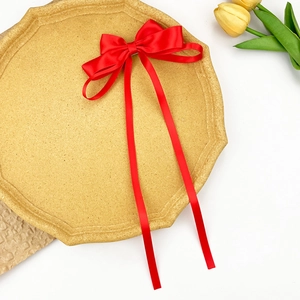 Detail of red satin bow hair clip with long ribbons on a decorative display tray