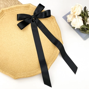 Détail d'une grande barrette à cheveux en satin noir avec de longs rubans sur un plateau