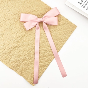 Close-up of pink satin ribbon hair clip with long streamers on textured background