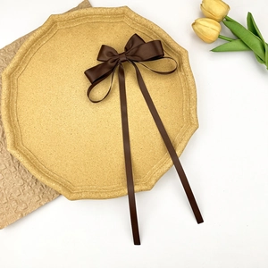 Detail view of a coffee brown satin bow hair clip with long ribbons on a tray
