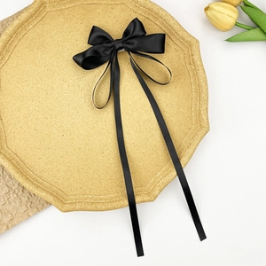 Detail of elegant black satin bow hair clip with long ribbons on a textured plate