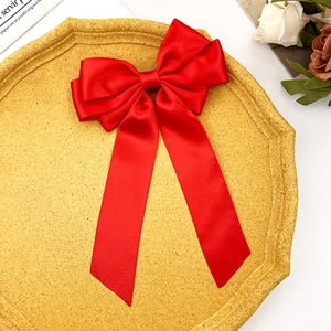 Detail of a large red satin bow hair clip with elegant long ribbons on a gold tray