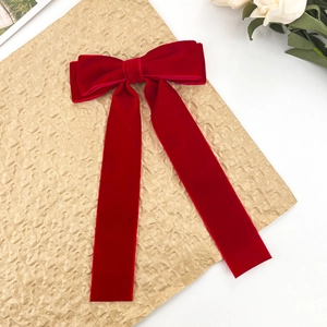 Macro detail of red velvet bow hair clip with long streamers on a textured gold background