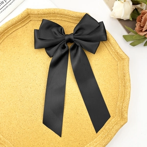 Elegant black satin bow hair clip with long ribbons on a yellow decorative tray