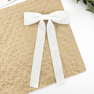 Detailed view of white velvet bow hair clip with long ribbons on textured paper