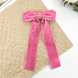 Detail view of a pink velvet bow hair clip with long ribbons on a textured surface