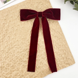 Macro detail of wine red velvet bow hair clip with long ribbons on a vintage surface