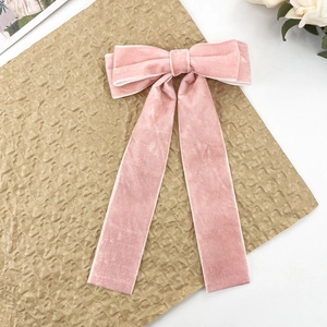 Detailed close-up of pink velvet bow hair clip with long streamers on textured paper